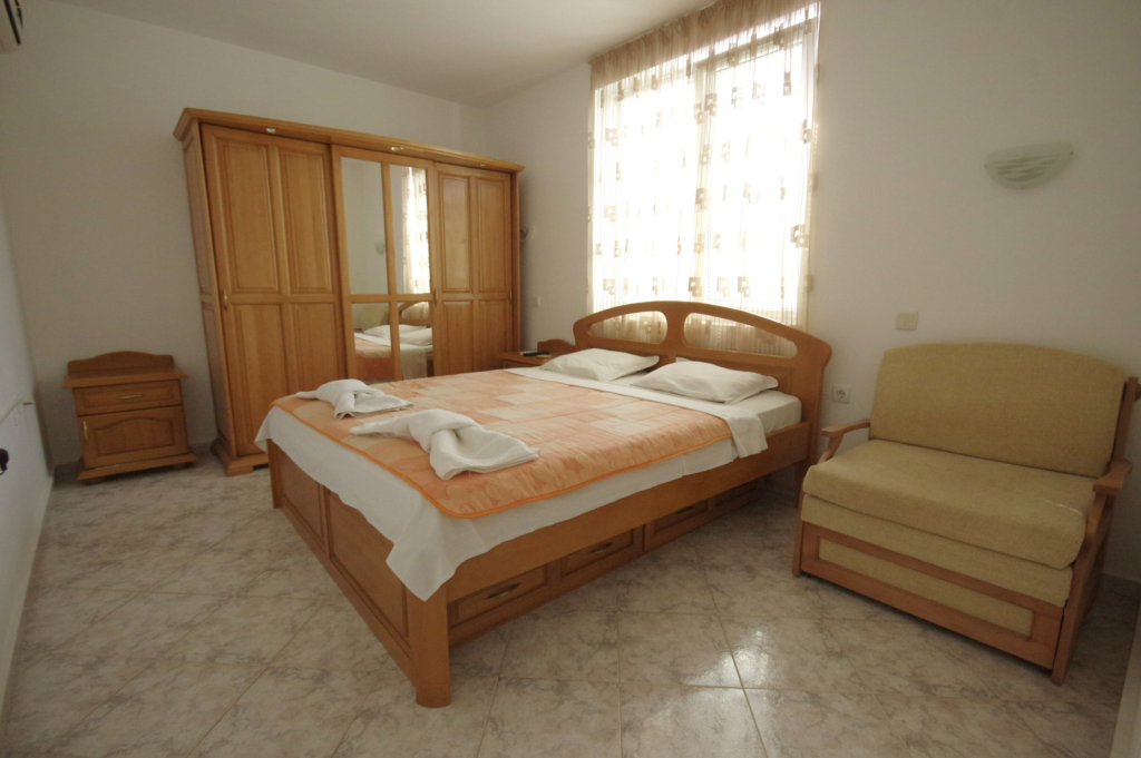 Bedroom 1 in Apartment 1 with a King size bed in the middle of the room, a single sofa bed to the right of the bed, a wardrobe along the left wall, a cable TV and air-conditioning.