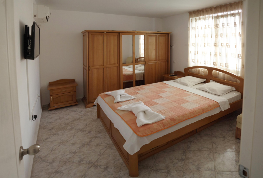 Bedroom 1 in Apartment 1 with a King size bed in the middle of the room, a single sofa bed to the right of the bed, a wardrobe along the left wall, a cable TV and air-conditioning.