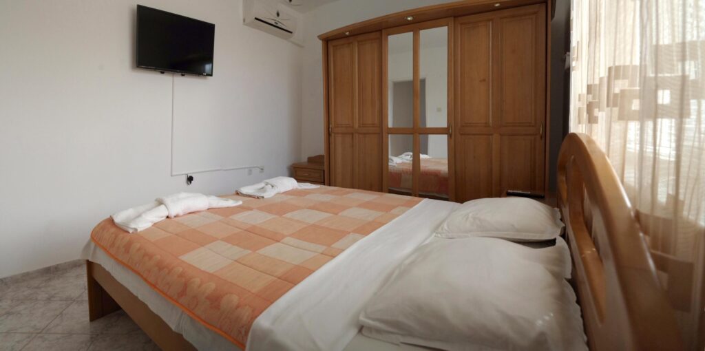 Bedroom 1 in Apartment 1 with a King size bed in the middle of the room, a single sofa bed to the right of the bed, a wardrobe along the left wall, a cable TV and air-conditioning.