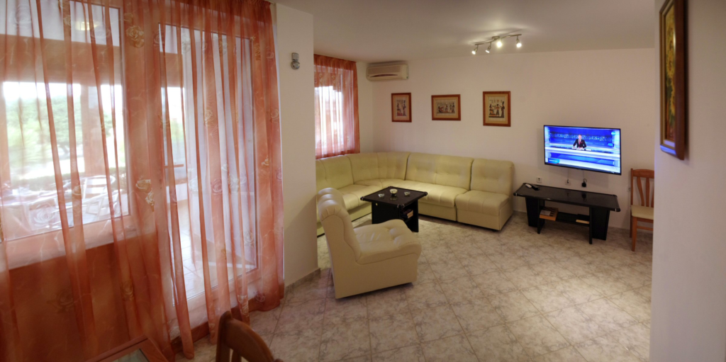 The spacious living Room in Apartment 1 with modular furniture that has a built in double bed and storage area, a coffee table, TV, separate dining area with an extendable table and 8 chairs. And an adjacent fully fitted kitchenette.