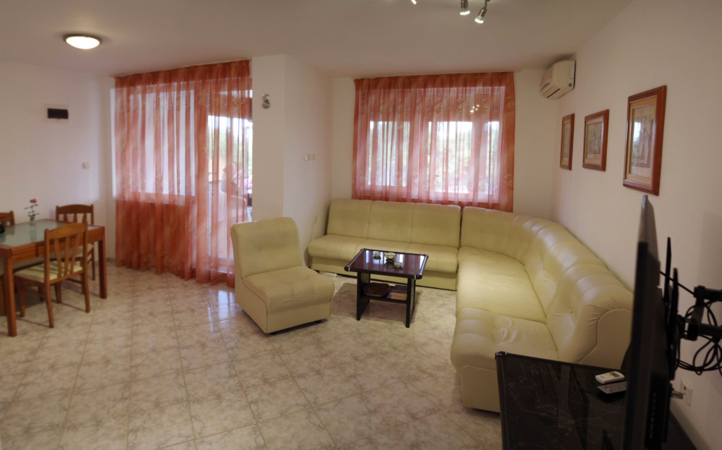 The spacious living Room in Apartment 1 with modular furniture that has a built in double bed and storage area, a coffee table, TV, separate dining area with an extendable table and 8 chairs. And an adjacent fully fitted kitchenette.