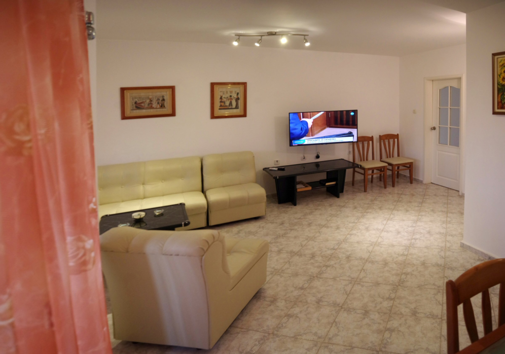 The spacious living Room in Apartment 1 with modular furniture that has a built in double bed and storage area, a coffee table, TV, separate dining area with an extendable table and 8 chairs. And an adjacent fully fitted kitchenette.