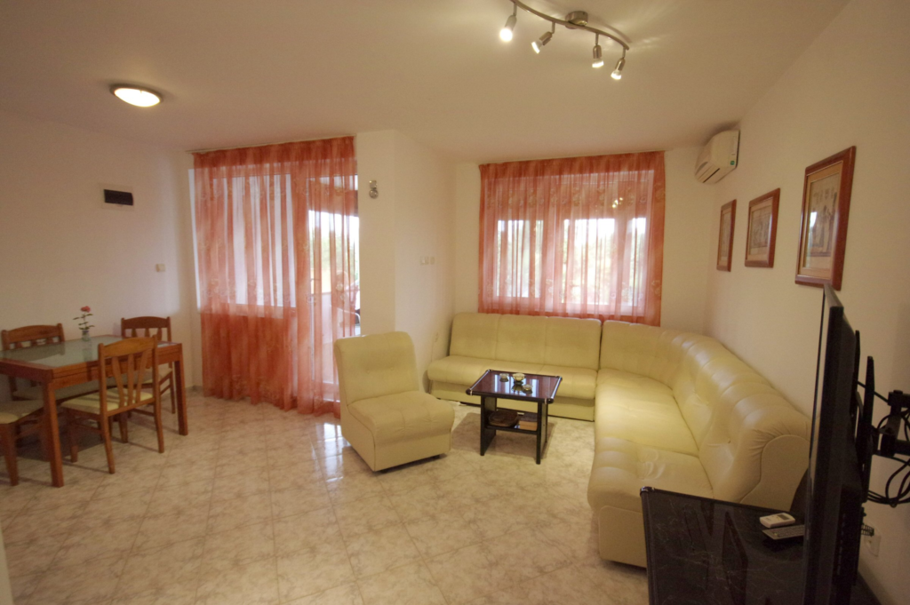 The spacious living Room in Apartment 1 with modular furniture that has a built in double bed and storage area, a coffee table, TV, separate dining area with an extendable table and 8 chairs. And an adjacent fully fitted kitchenette.