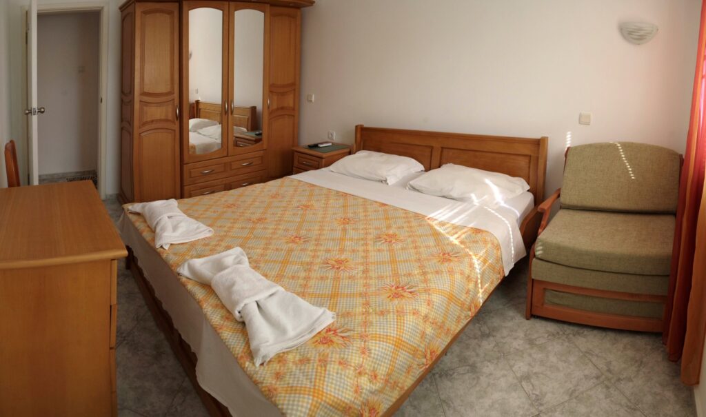 Bedroom 1 in Apartment 2 with a King size bed in the middle of the room, a single sofa bed to the right of the bed, a wardrobe along the left wall, a cable TV and air-conditioning.