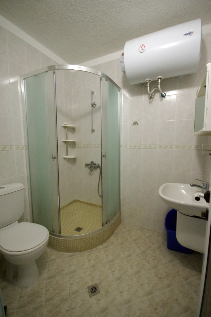 Bathroom 1 in Apartment 2 with a shower cabin, sink, toilet and a toiletries cabinet.
