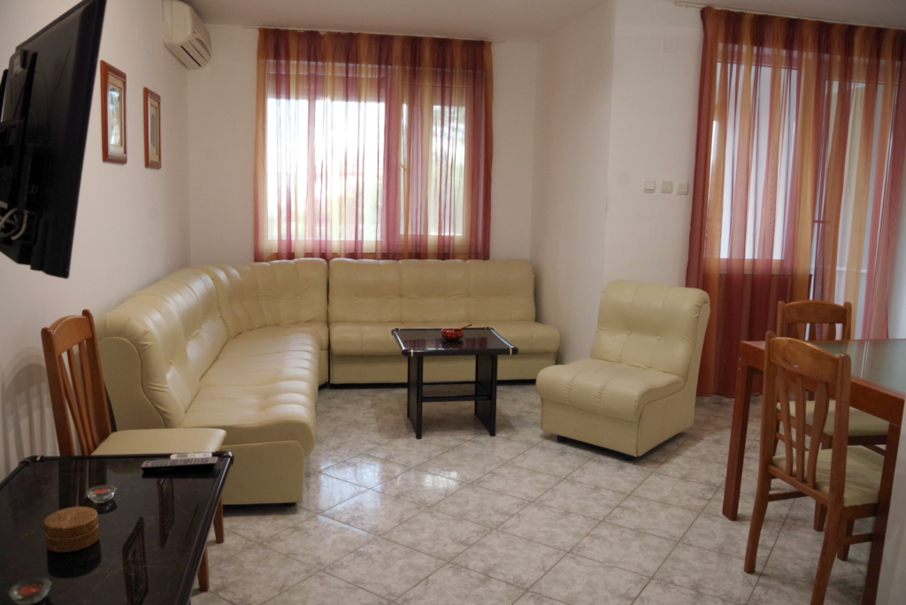 The spacious living Room in Apartment 2 with modular furniture that has a built in double bed and storage area, a coffee table, TV, separate dining area with an extendable table and 8 chairs. And an adjacent fully fitted kitchenette.