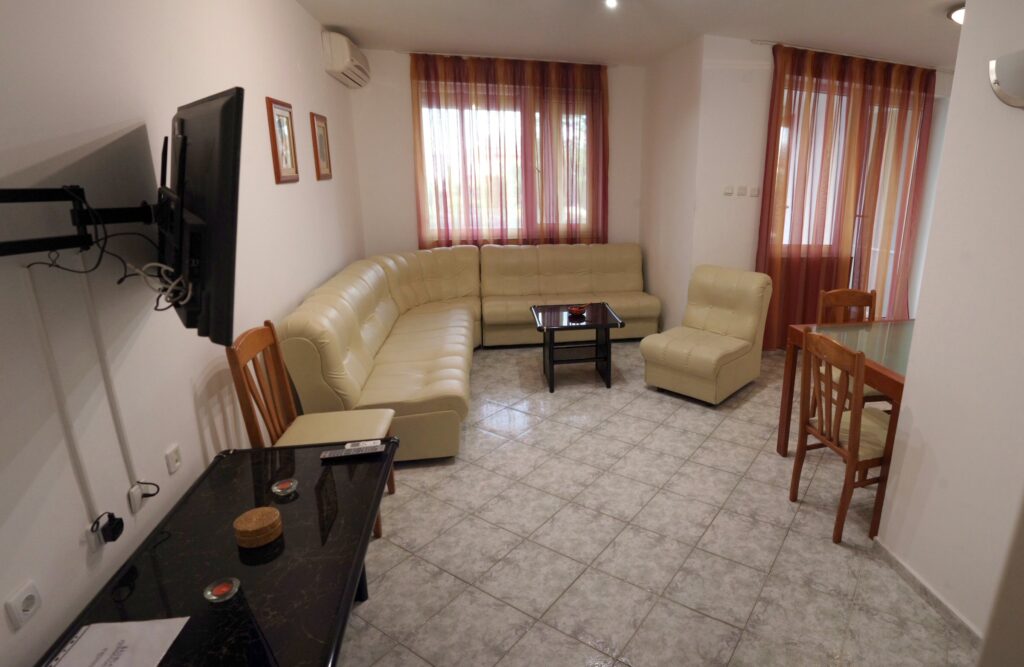 The spacious living Room in Apartment 2 with modular furniture that has a built in double bed and storage area, a coffee table, TV, separate dining area with an extendable table and 8 chairs. And an adjacent fully fitted kitchenette.