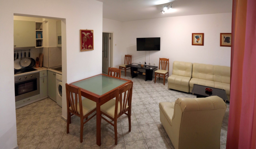 The spacious living Room in Apartment 2 with modular furniture that has a built in double bed and storage area, a coffee table, TV, separate dining area with an extendable table and 8 chairs. And an adjacent fully fitted kitchenette.