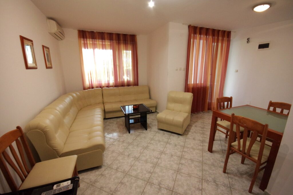 The spacious living Room in Apartment 2 with modular furniture that has a built in double bed and storage area, a coffee table, TV, separate dining area with an extendable table and 8 chairs. And an adjacent fully fitted kitchenette.