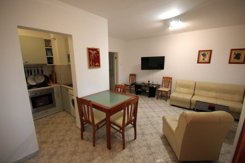 The spacious living Room in Apartment 2 with modular furniture that has a built in double bed and storage area, a coffee table, TV, separate dining area with an extendable table and 8 chairs. And an adjacent fully fitted kitchenette.