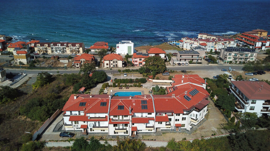 A Birds Eye view of Summer Romantica Apartments and the complex space they are located at. Shows the big private pool area that includes a children's pool, lounge chairs, the private parking space and the sea view and beach that are a short walking distance from the complex.